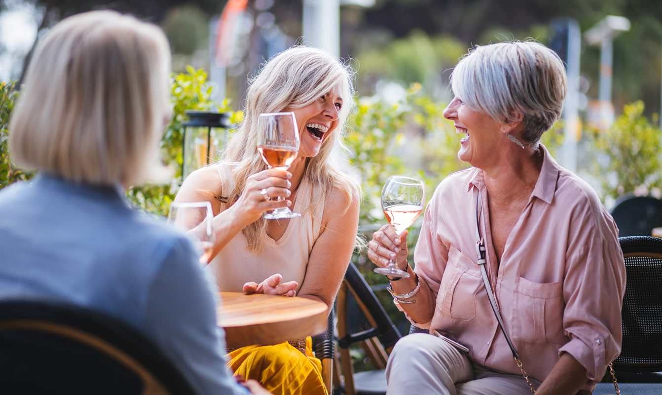 Reife Frauen genießen ein Glas Wein, haben Spaß und lachen gemeinsam in einem Restaurant in der Stadt.