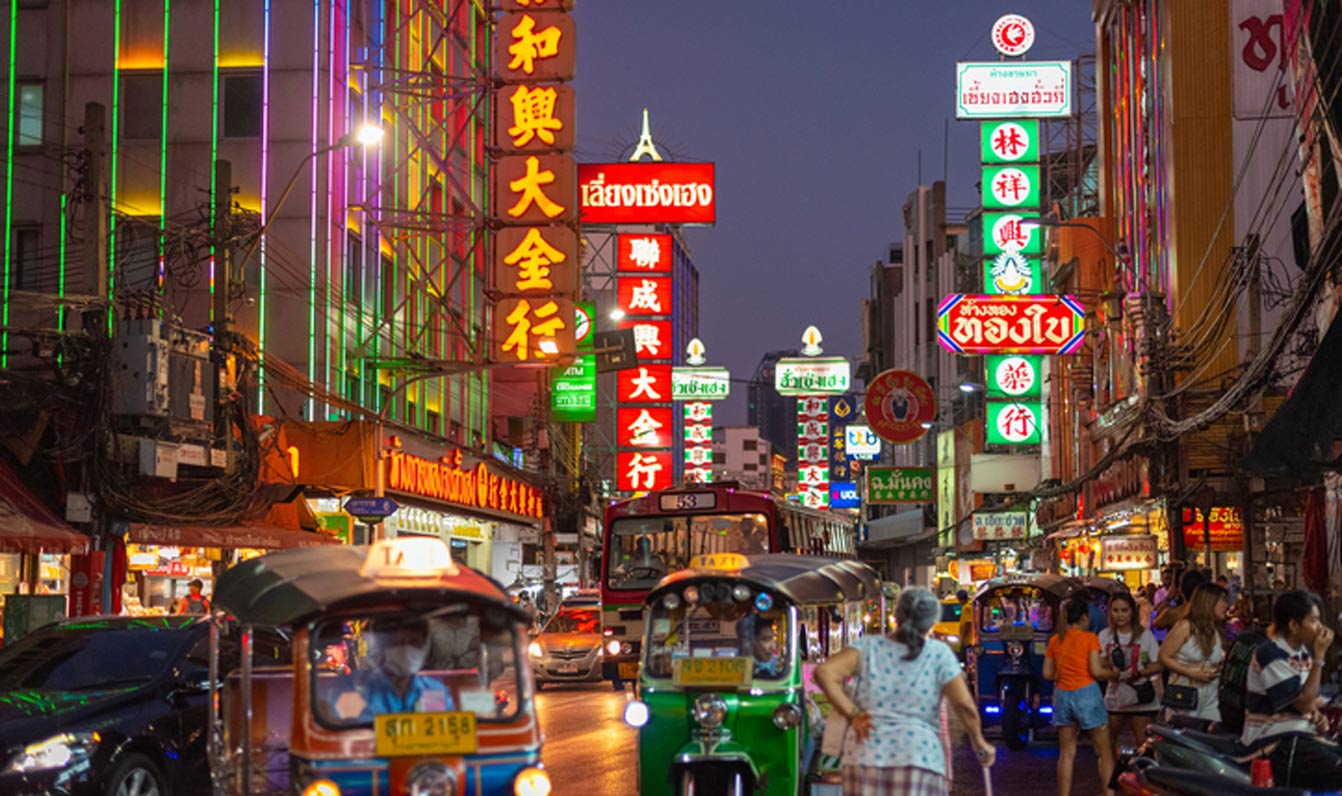 Bangkok, Thailand – 27. März 2023: Die Yaowarat Road bei Nacht mit chinesischen Schildern, Straßenverkehr und Passanten.