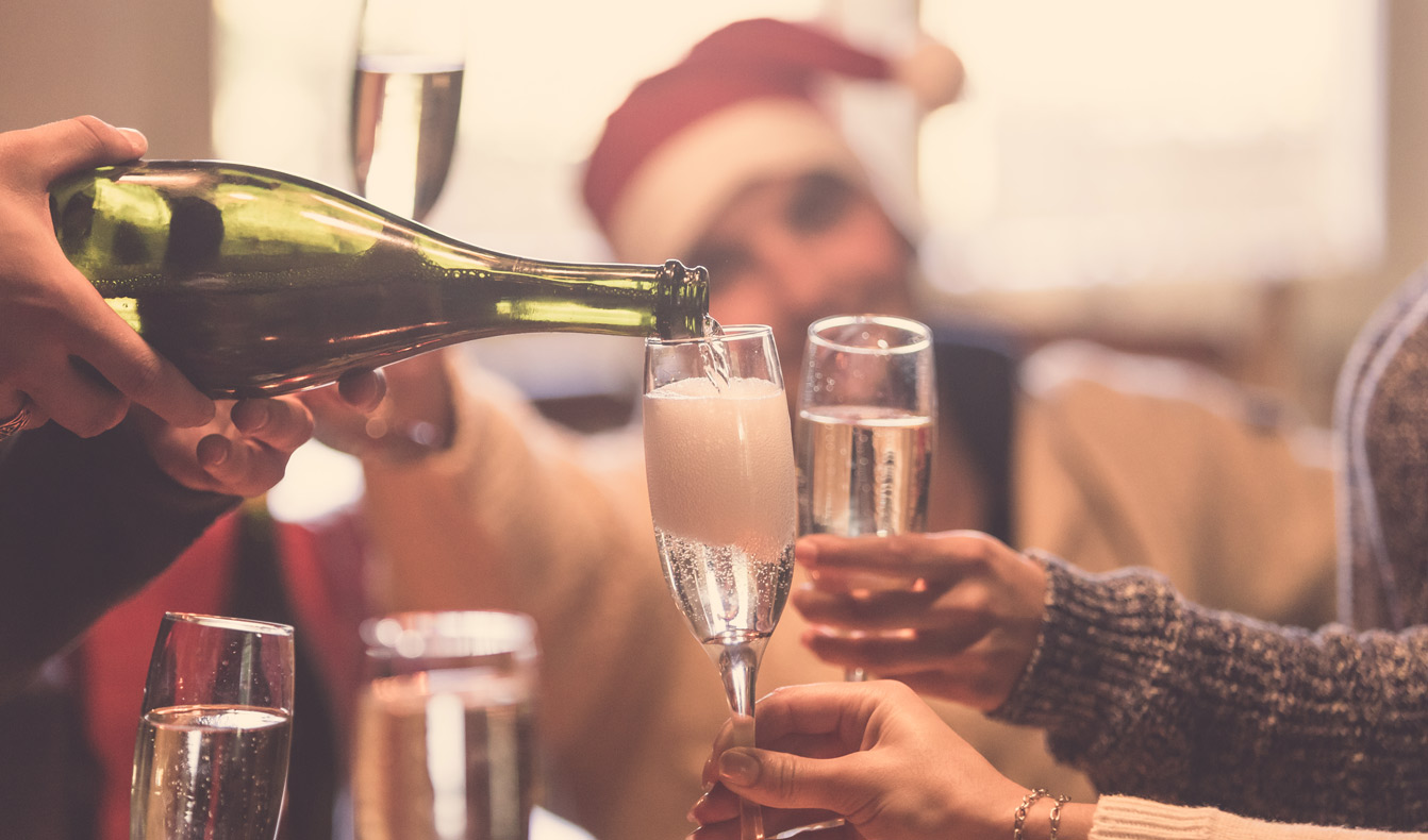 Ausschnitt eines Bildes, auf dem Menschen mit Sekt anstoßen und Weihnachten feiern. Symbolbild Wein an Weihnachten