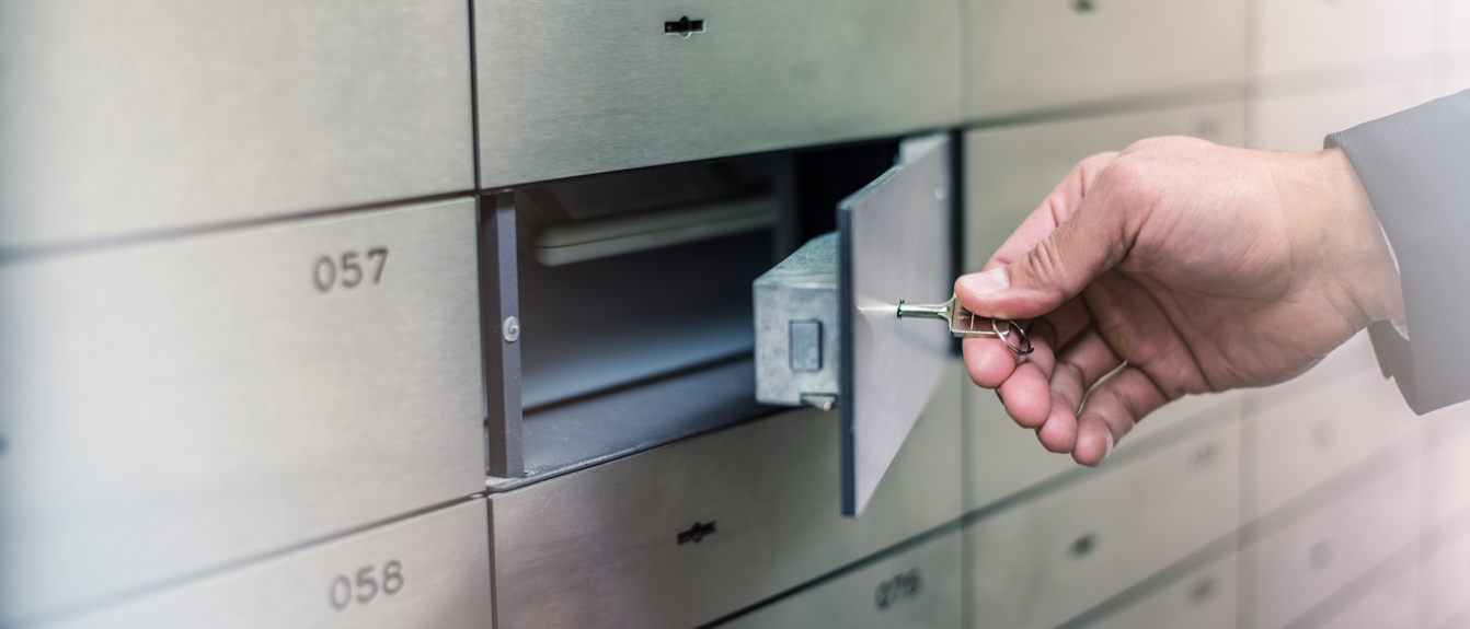 Close up of a hand holding a key that is attached to a small open vault door.