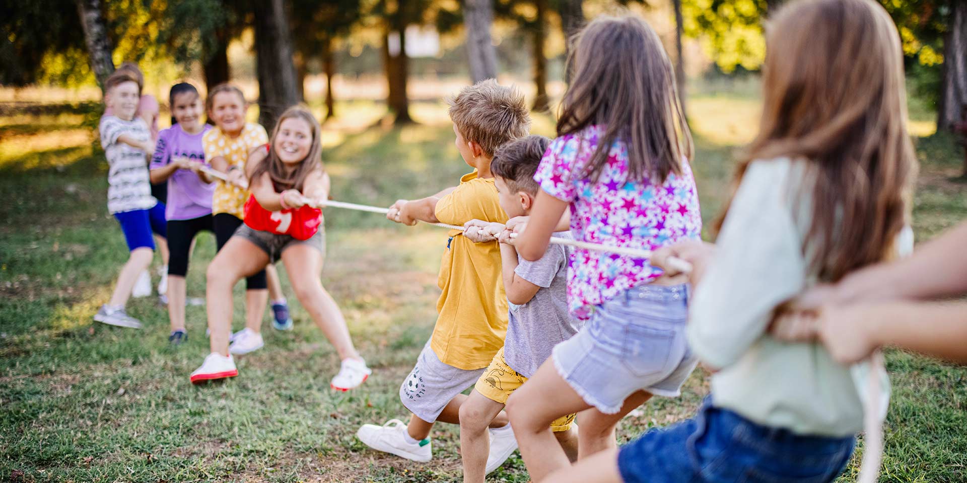 large group of playful kids having fun in the park while playing tug-of-war.