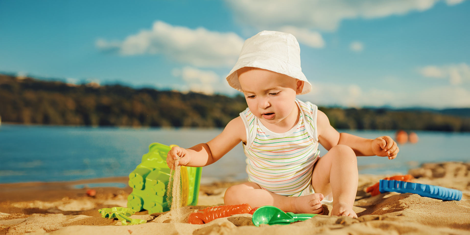 cute baby boy playing with beach toys on tropical beach.