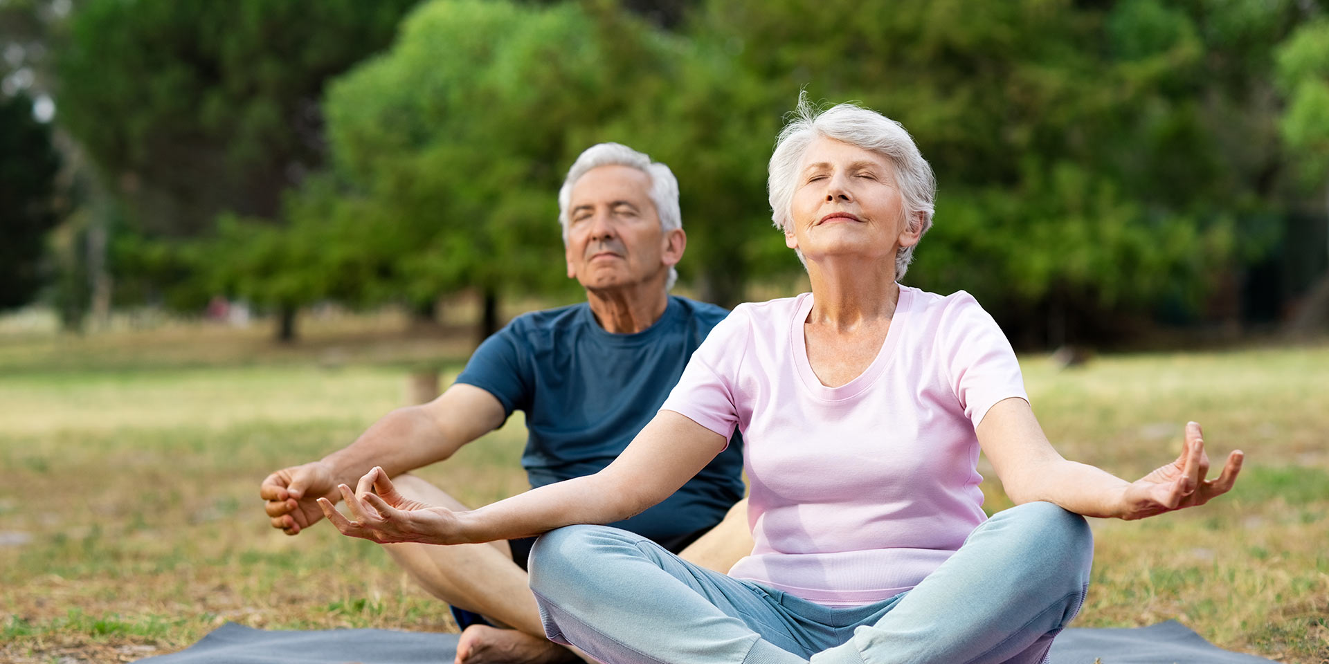 old couple relaxing while sitting in lotus pose. senior man and elly man meditating sitting in lotus position at park with closed eyes. aged man and man feeling relaxed sitting on yoga mat.