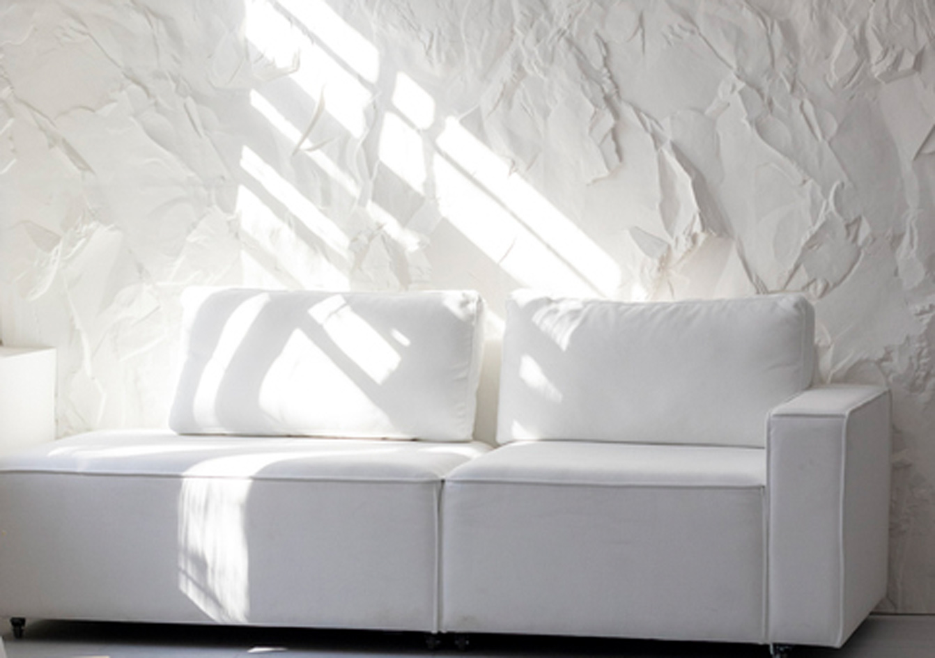 Ein weißes Sofa vor einer weißen, strukturierten Wand. Innenarchitektur im Stil des Minimalismus.
