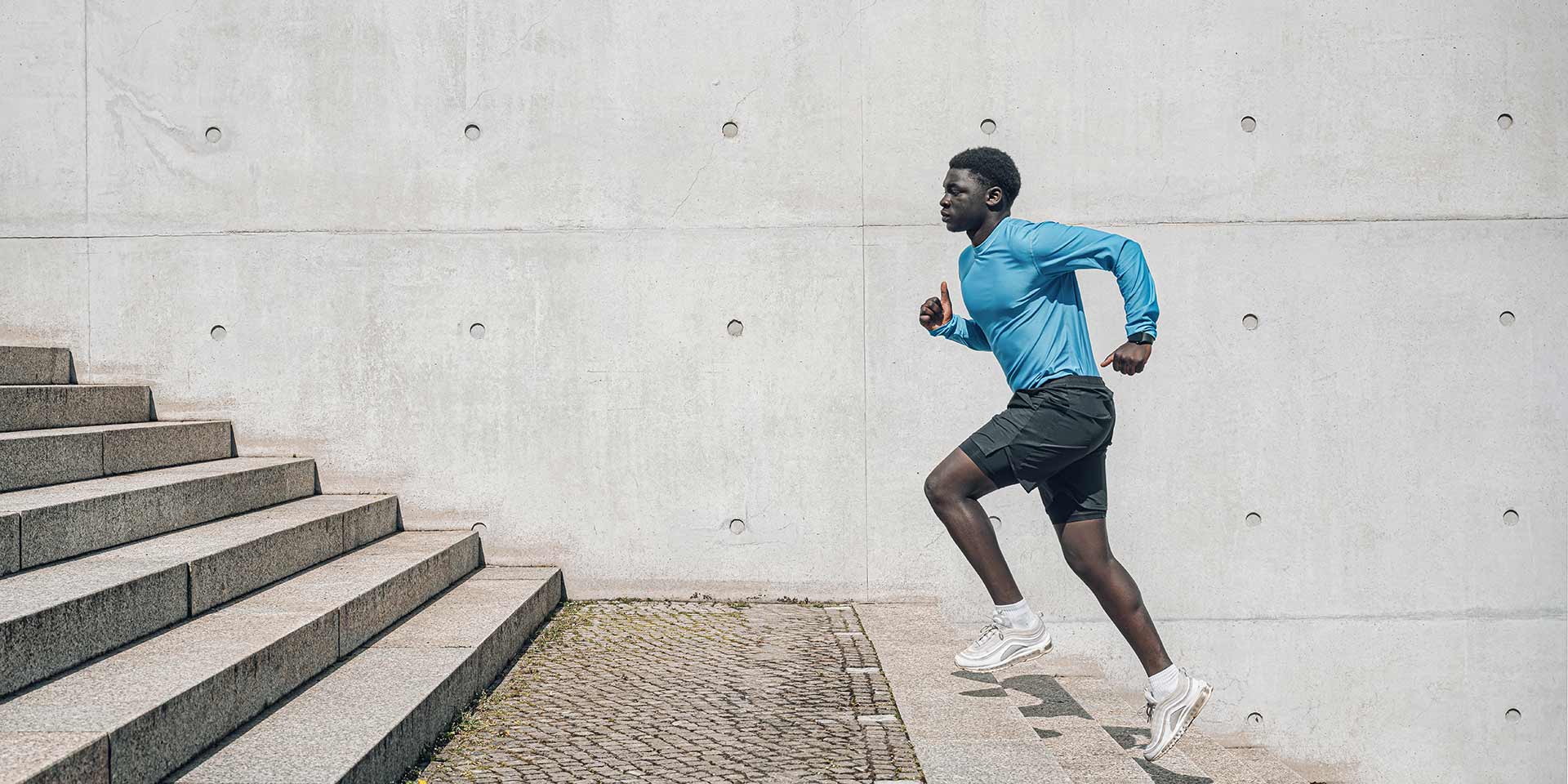 young sportsman running up steps in front of concrete wall outdoors in berlin at sunny day