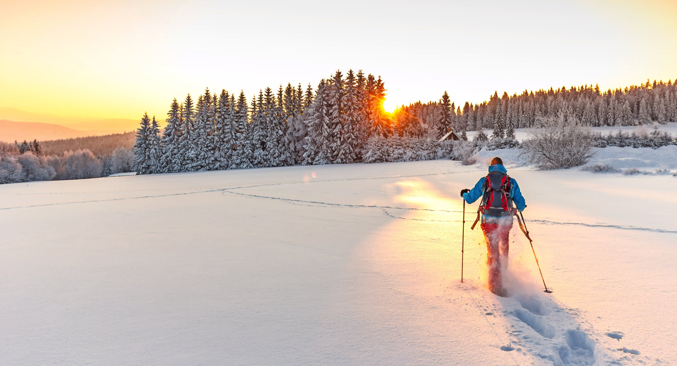 Eine Person auf einer Schneeschuhtour bei Sonnenuntergang