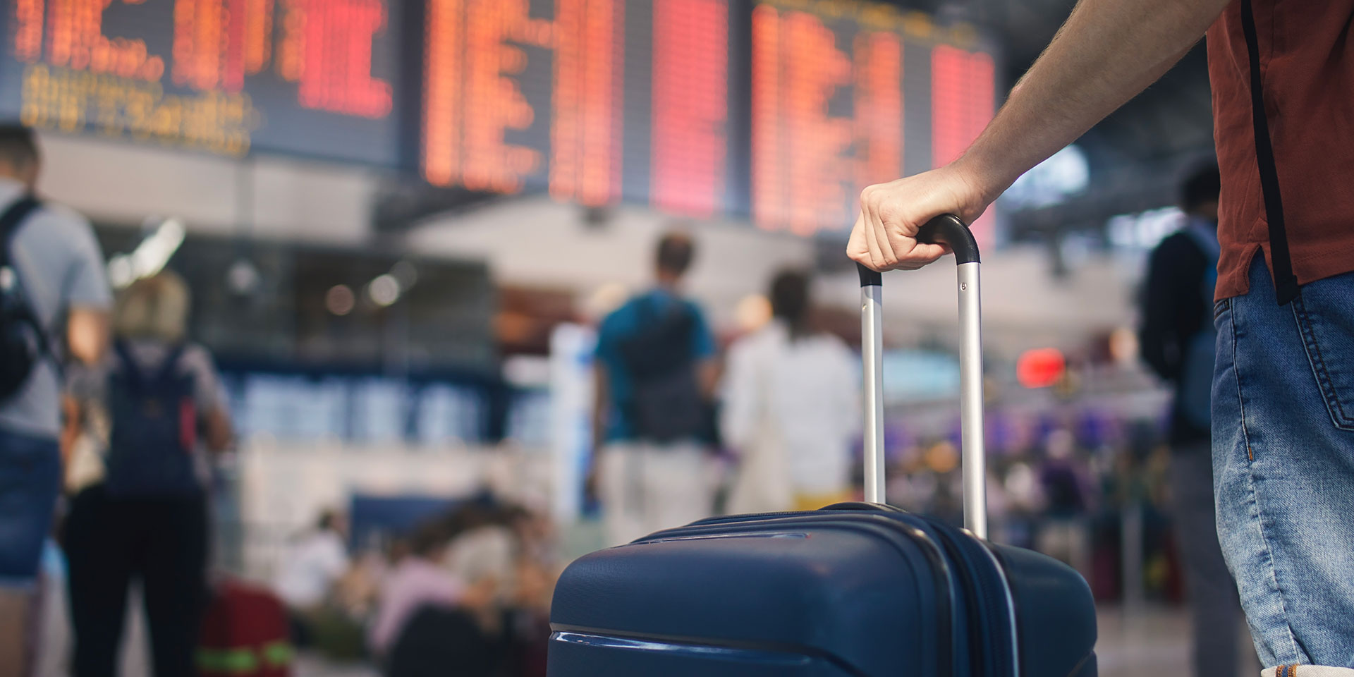 traveling by airplane. man waiting in airport terminal. selective focus on hand holding suitcase against arrival and departure board. passenger is ready for travel.